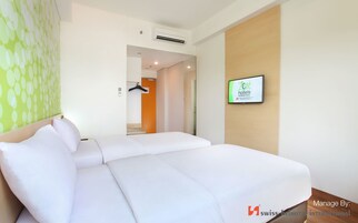 A hotel room with a bed, a wall-mounted TV, and a door leading to a bathroom.