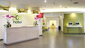 Un espace d’accueil d’hôtel avec un comptoir de réception blanc, un écran numérique et un mur vert.