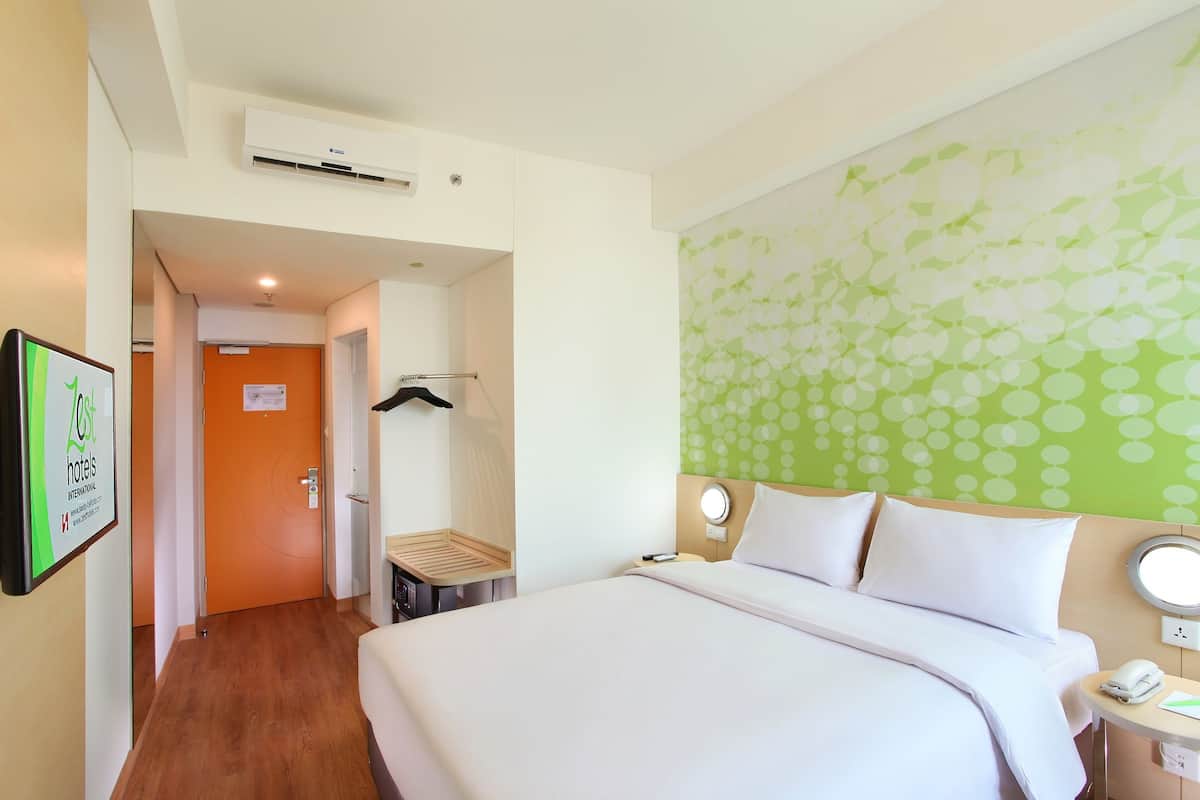 A hotel room with a bed, bedside table, and a wall-mounted air conditioner.