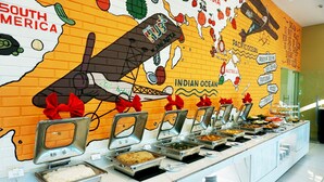 Un buffet proposant une variété de plats et un mur décoré d’une fresque représentant une carte avec un avion et un ruban rouge.
