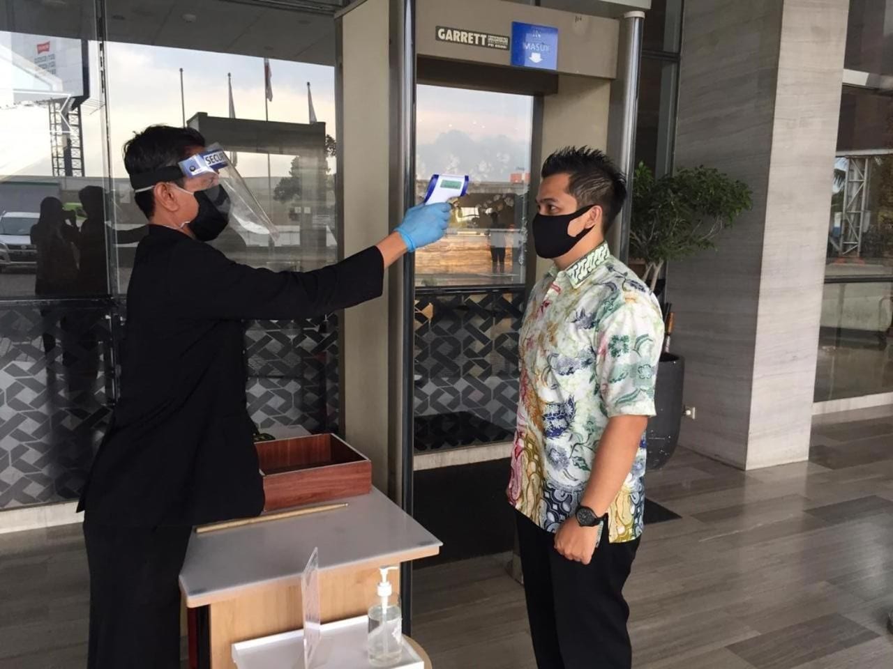 A person being screened at a security checkpoint with a metal detector and a blue handheld device.