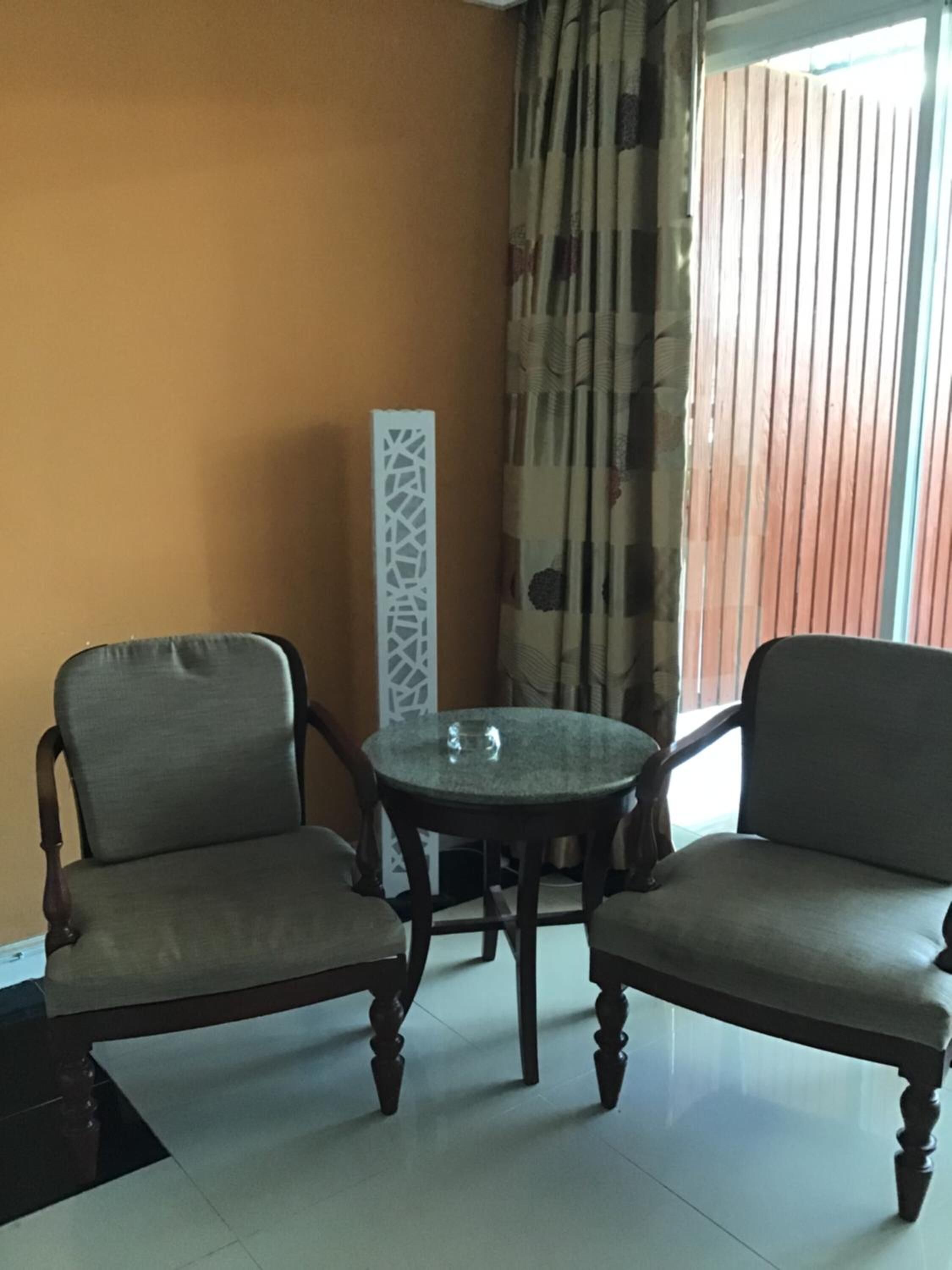 A room with two upholstered chairs, a small round table, and a decorative white panel on the wall.