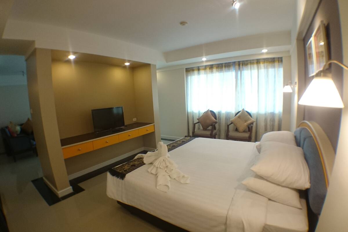 A hotel room with a bed, a desk with a TV, two armchairs, and a window with curtains.