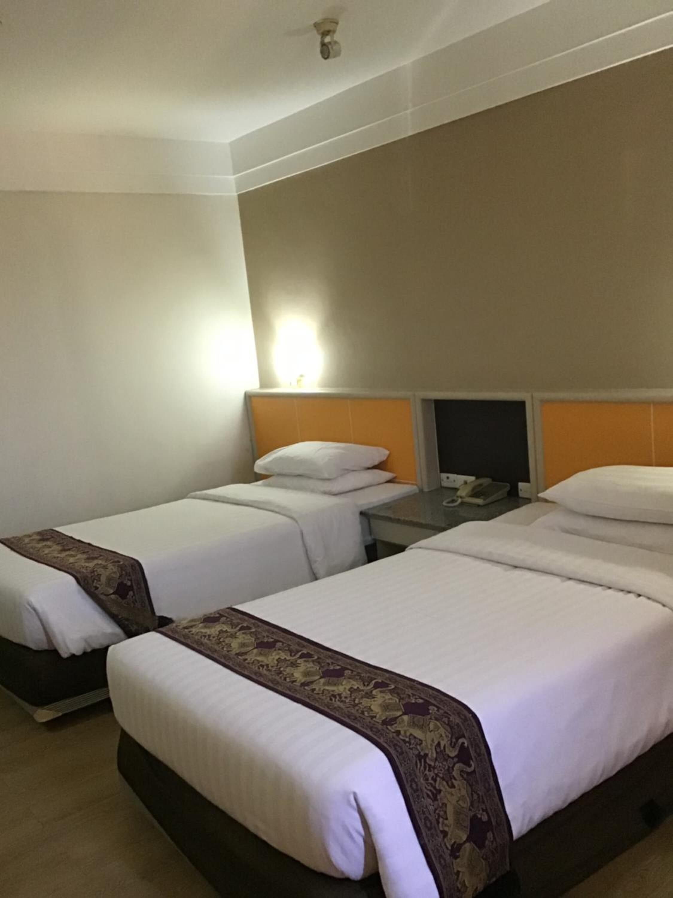 A hotel room with two single beds, each with a headboard and a bedside table.