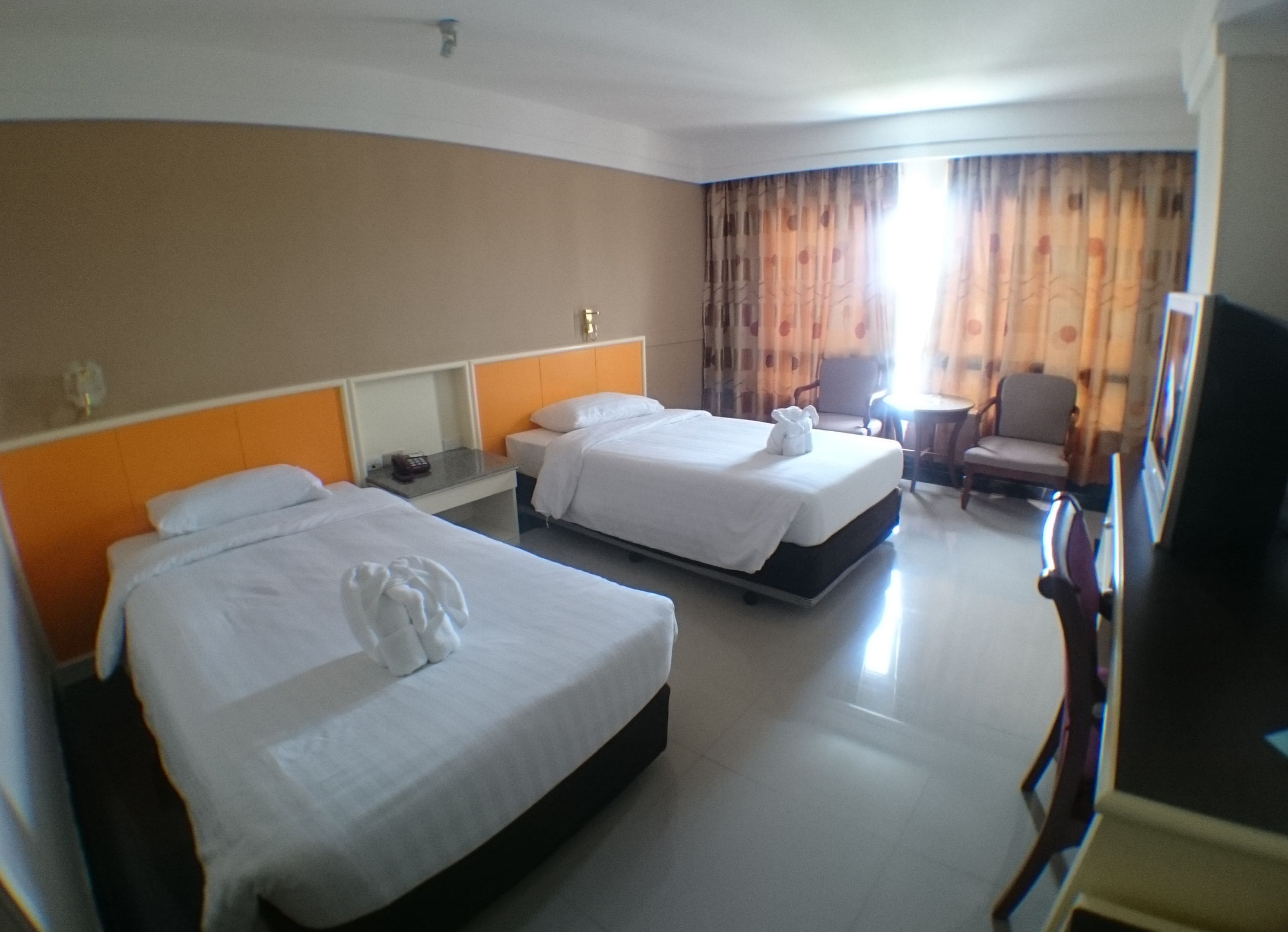 A hotel room with two beds, a small table, a chair, and a TV.