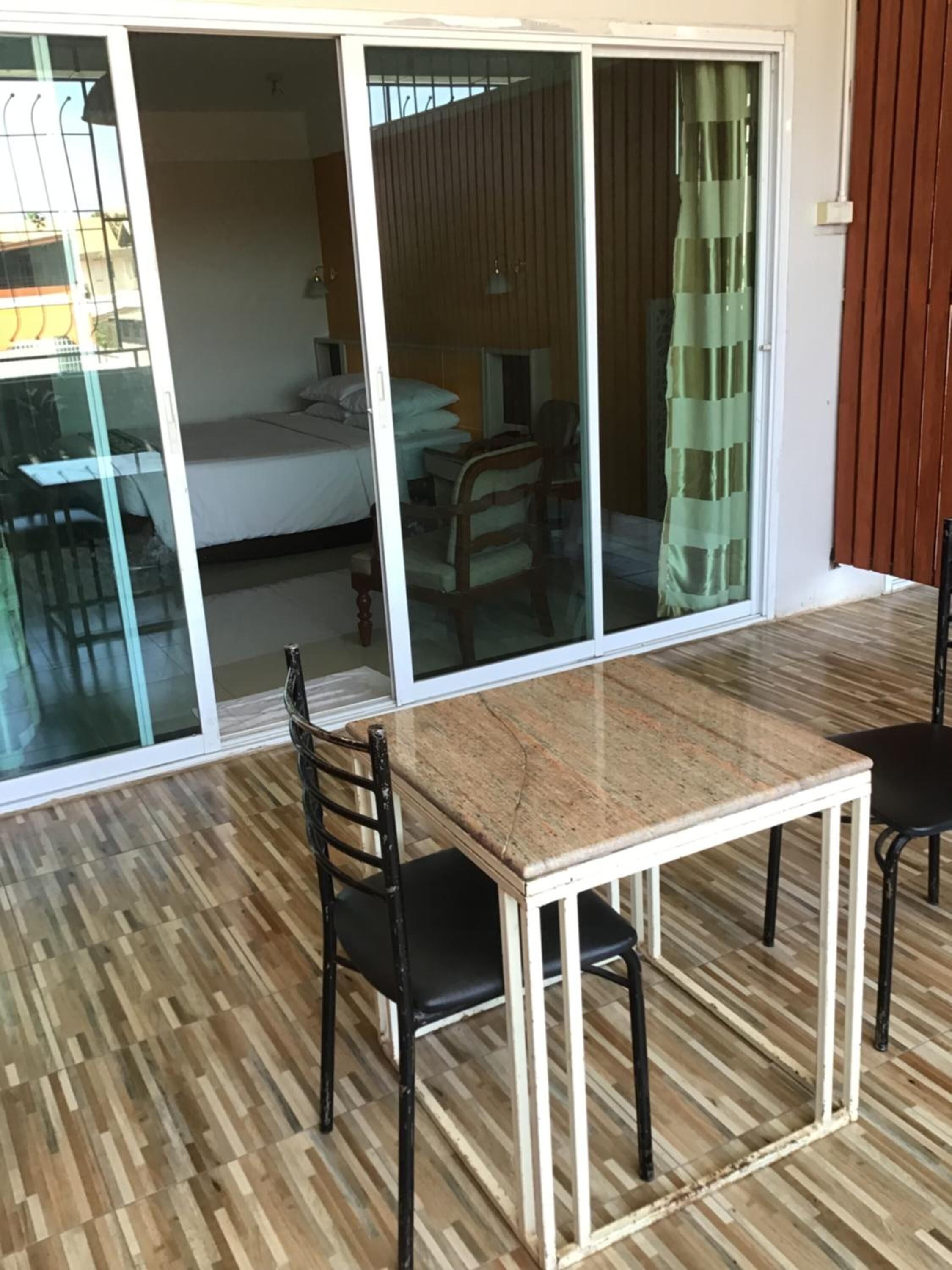 Ein Zimmer mit einer Schiebetür zum Balkon, Holzboden, einem Tisch mit Stühlen und einem Bett mit Fenster.