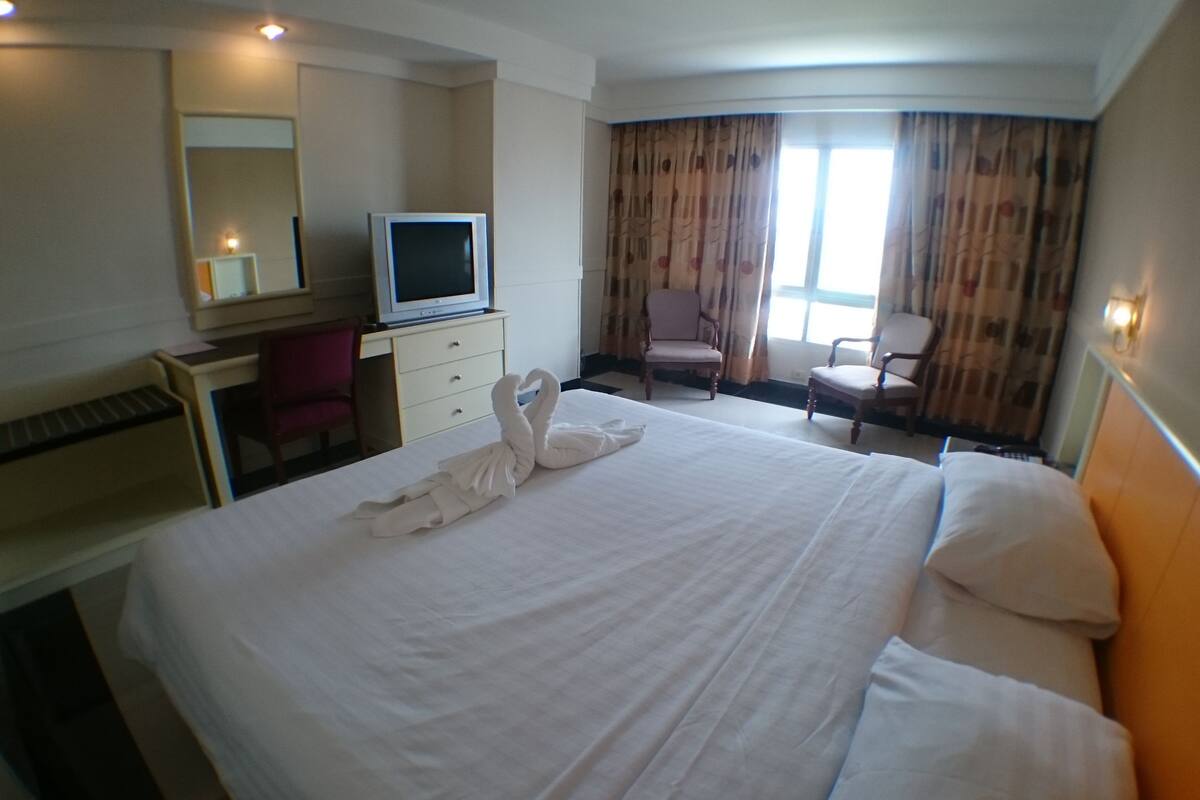 A hotel room with a large bed, a desk with a television, a chair, and a window with curtains.