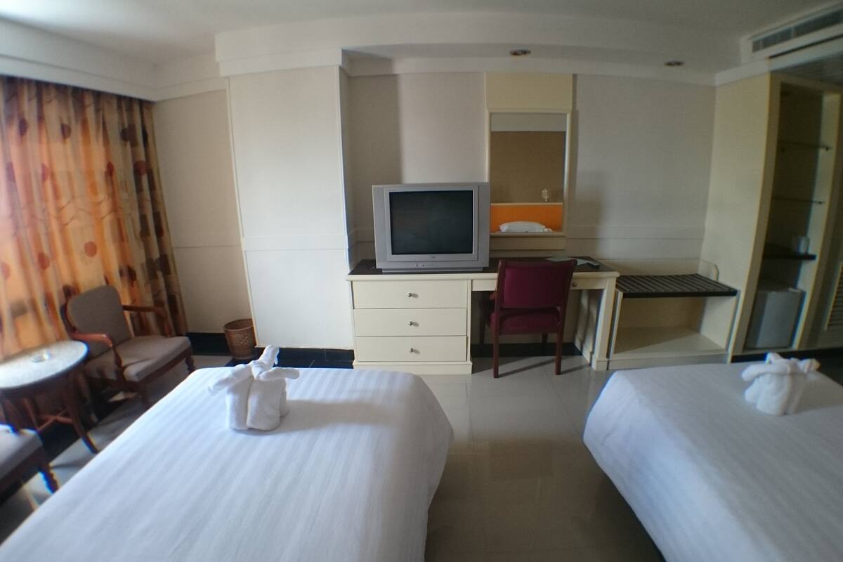 A hotel room with two beds, a desk with a computer, a television, a chair, and a small table.