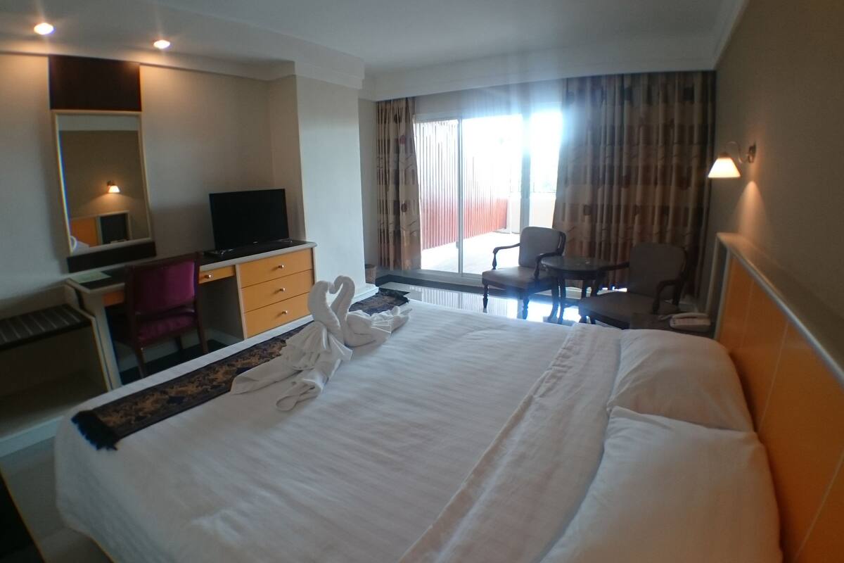 A hotel room with a large bed, a desk with a computer, a chair, and a TV.