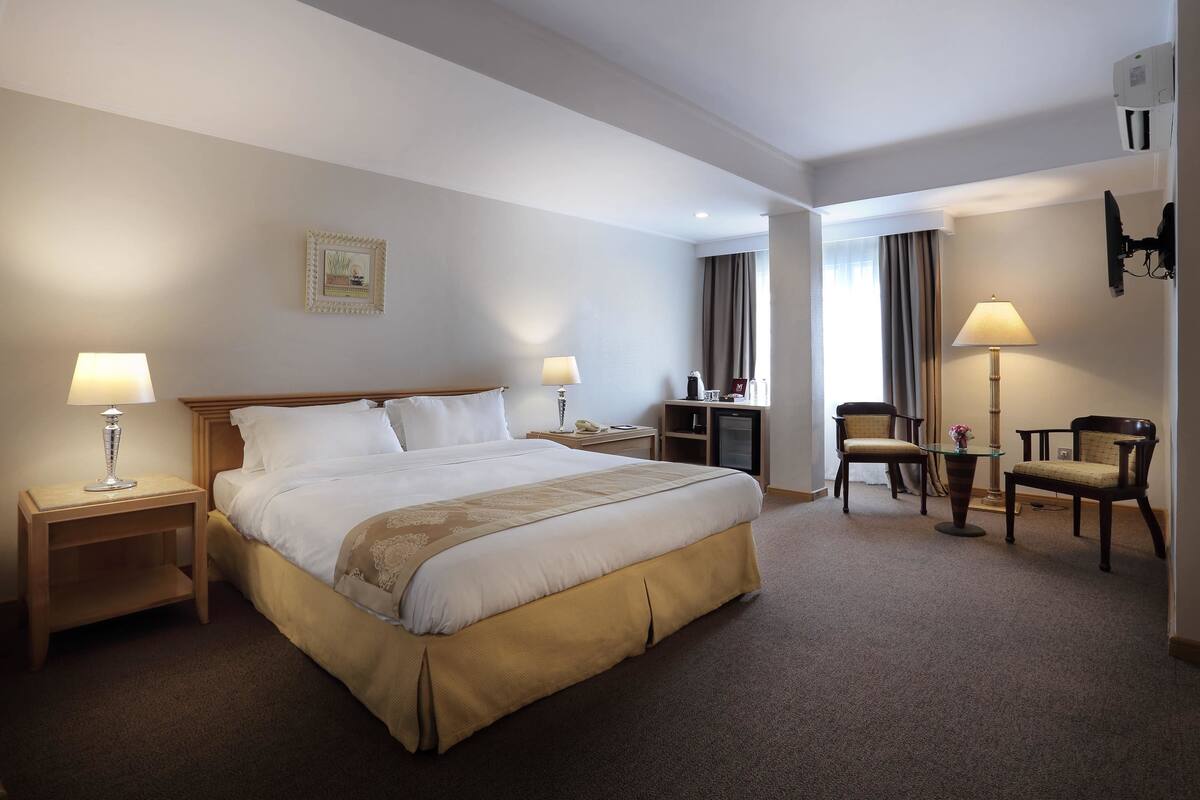 A hotel room with a large bed, two bedside tables with lamps, a desk with a chair, and a TV mounted on the wall.
