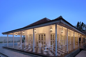 A covered outdoor seating area with tables and chairs, a checkered floor, and hanging lights. - Menumbing Heritage Hotel (Pangkalpinang)