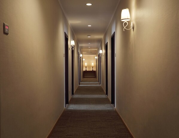 A hotel hallway with carpeted floors, wall-mounted light fixtures, and doors on both sides.