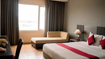Una habitación de hotel con cama, sofá, mesita de noche con lámpara y ventana con cortinas.