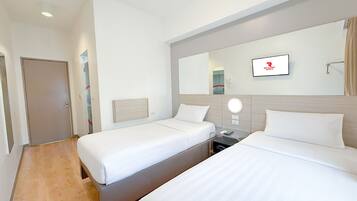 A hotel room with two single beds, a bedside table with a lamp, a mirror, and a wall-mounted TV.