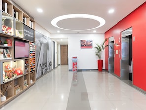 A modern hallway with a red accent wall, a large potted plant, and a digital display. - Red Planet Makati Amorsolo (Makati)