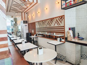 A restaurant interior with multiple tables and chairs, a patterned wall, and a shelf with beverages. - Red Planet Makati Amorsolo (Makati)