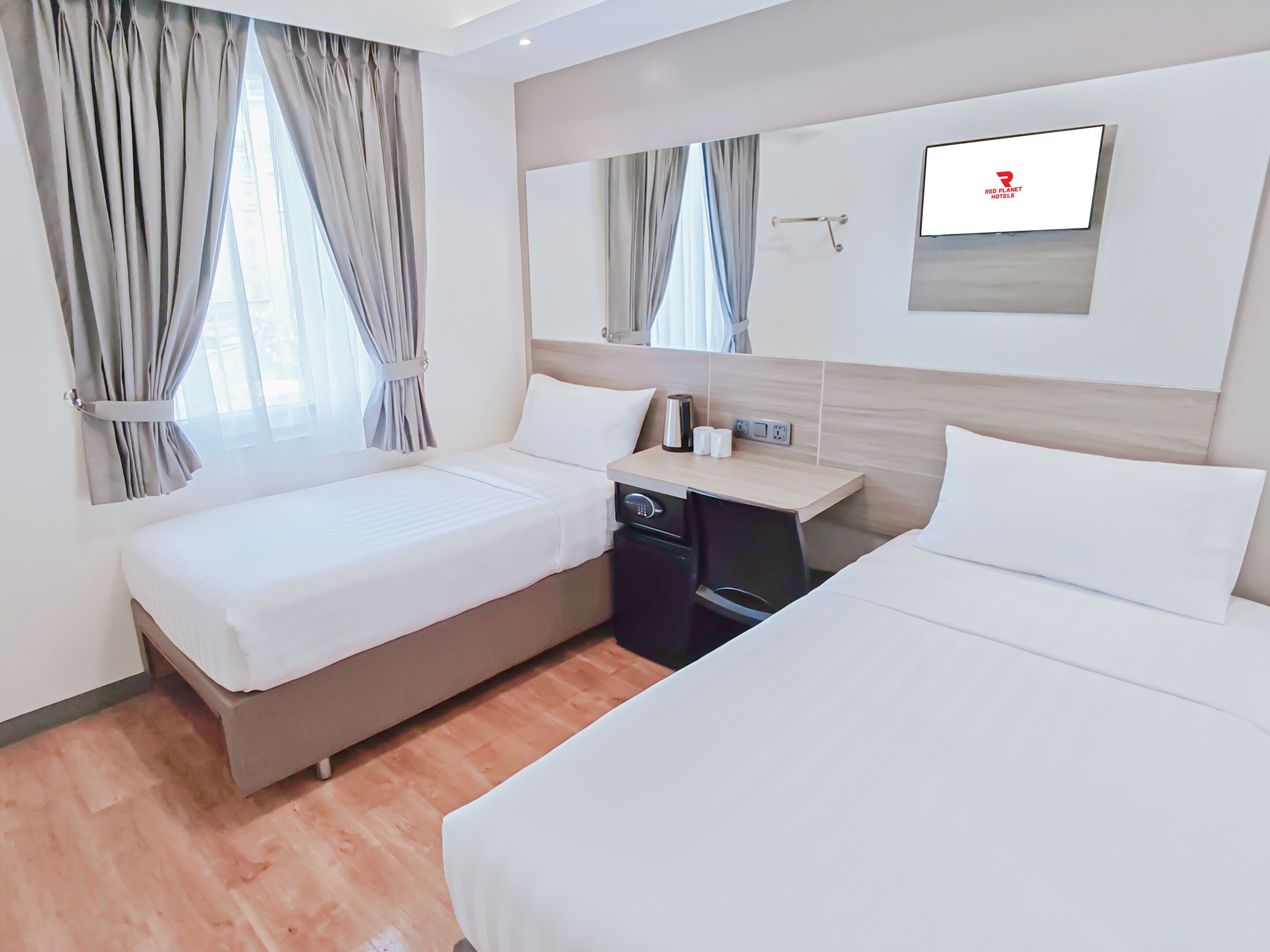 A hotel room with two beds, a small desk, a mirror, and a television.