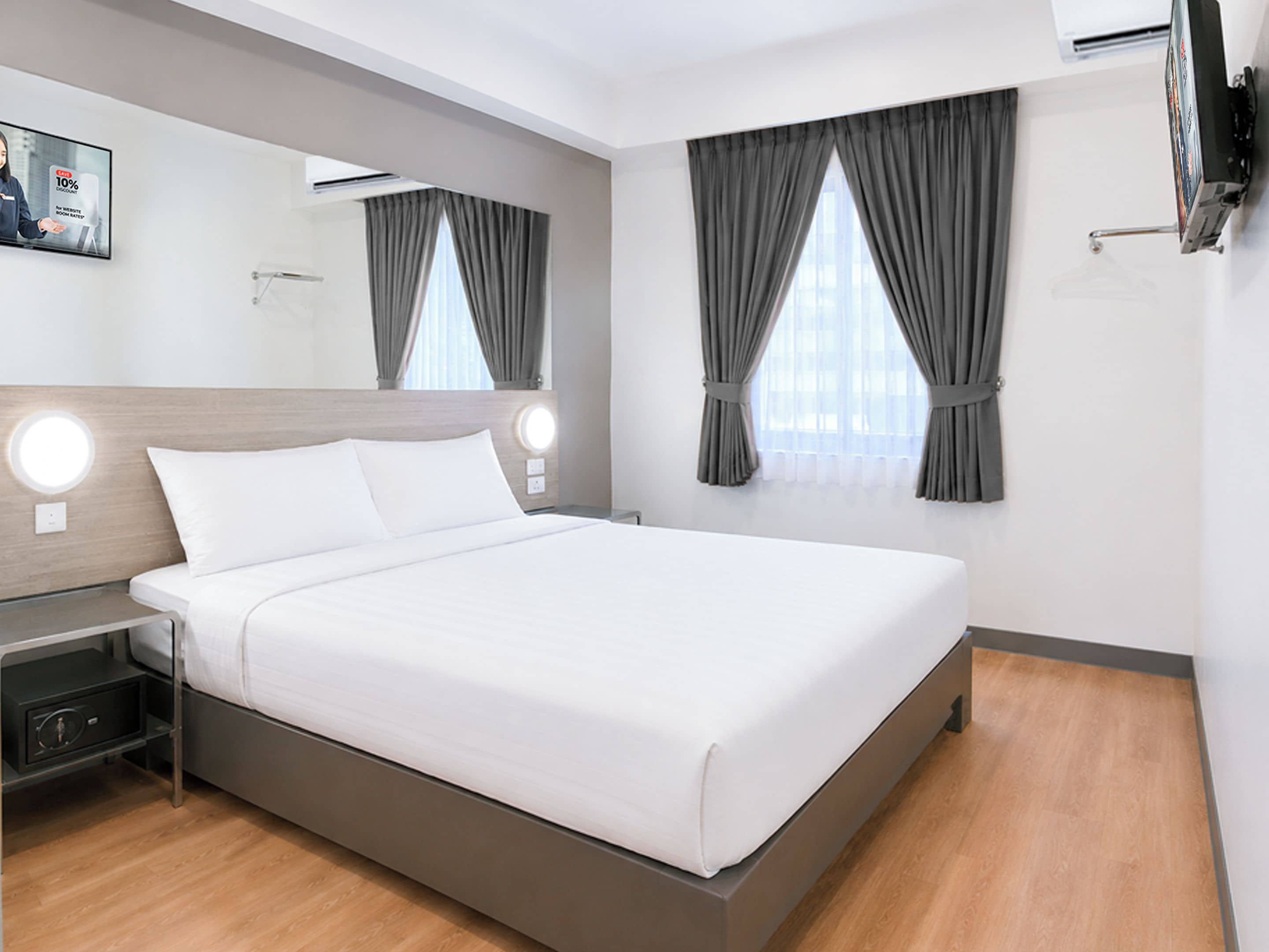 Ein modernes Hotelzimmer mit einem großen Bett, Nachttischen, einem Flachbildfernseher und einem Fenster mit Vorhängen.