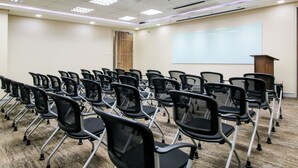 A conference room with rows of black chairs, a podium, and a projector screen on the wall. - Red Planet Makati Amorsolo (Makati)
