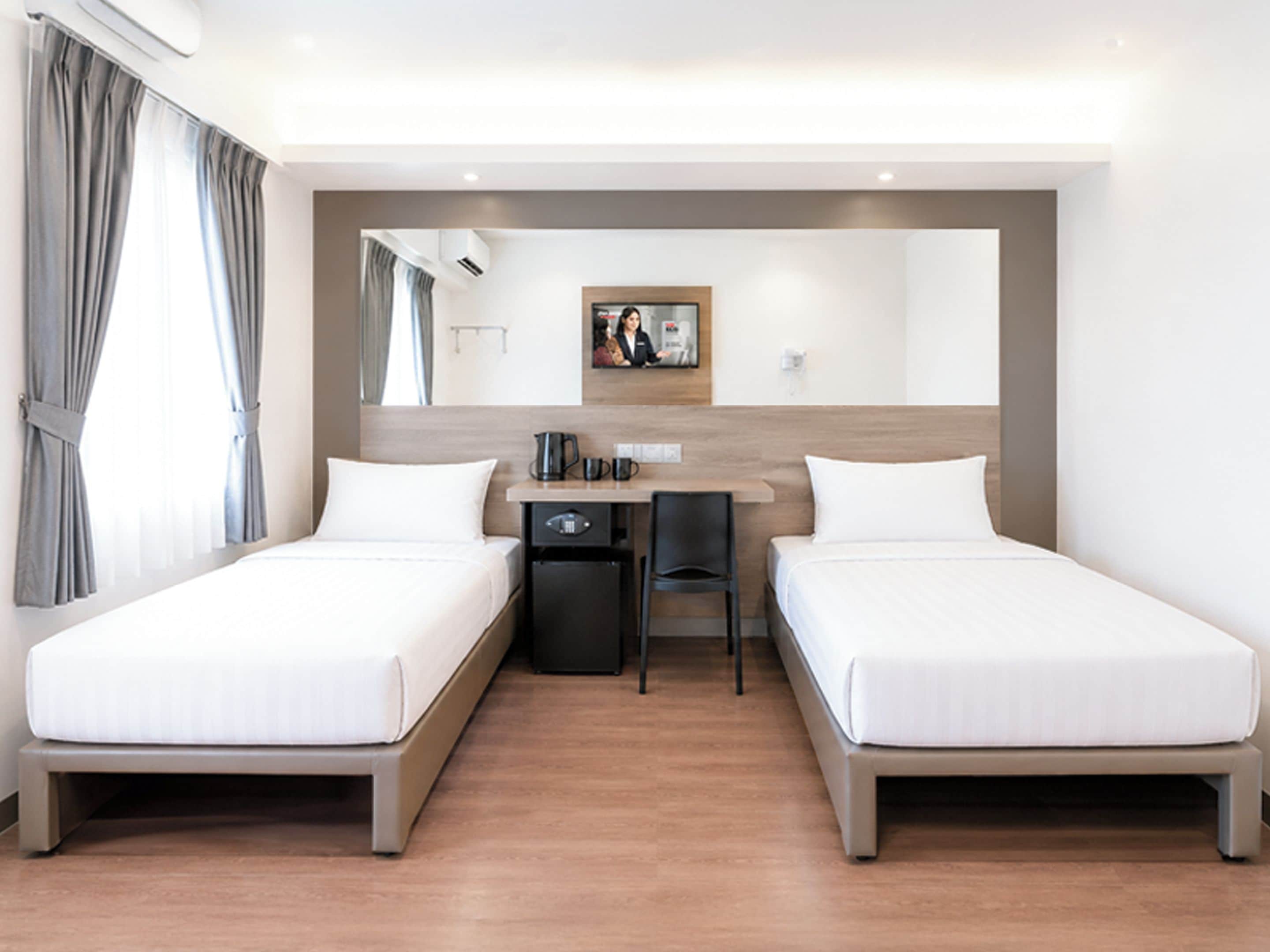 Habitación de hotel con dos camas individuales, un escritorio pequeño con una silla, cafetera y un cuadro en la pared.