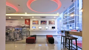 A modern reception area with a cityscape view, a counter with computers, and red seating. - Red Planet Makati Amorsolo (Makati)