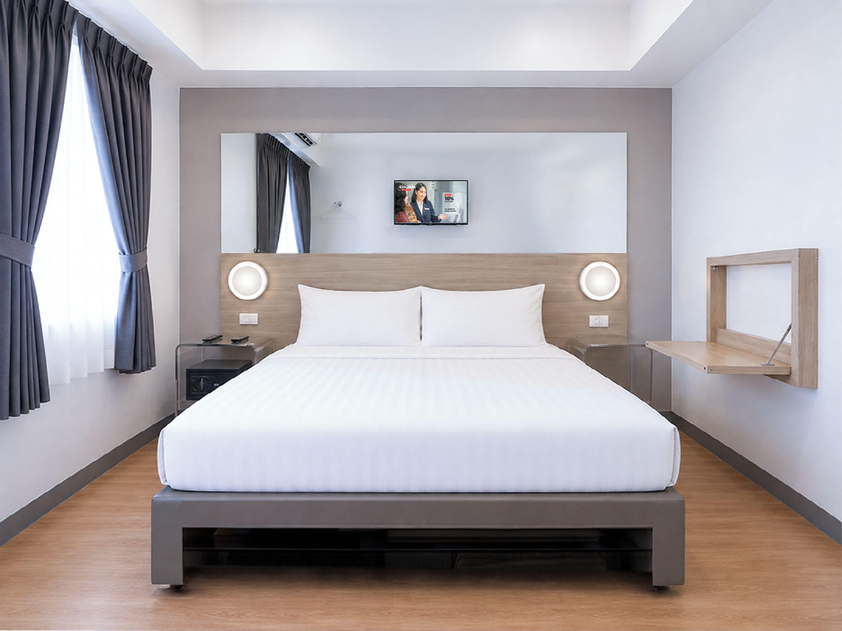Una camera d'albergo moderna con un letto grande, comodini, una TV a parete e una mensola in legno.
