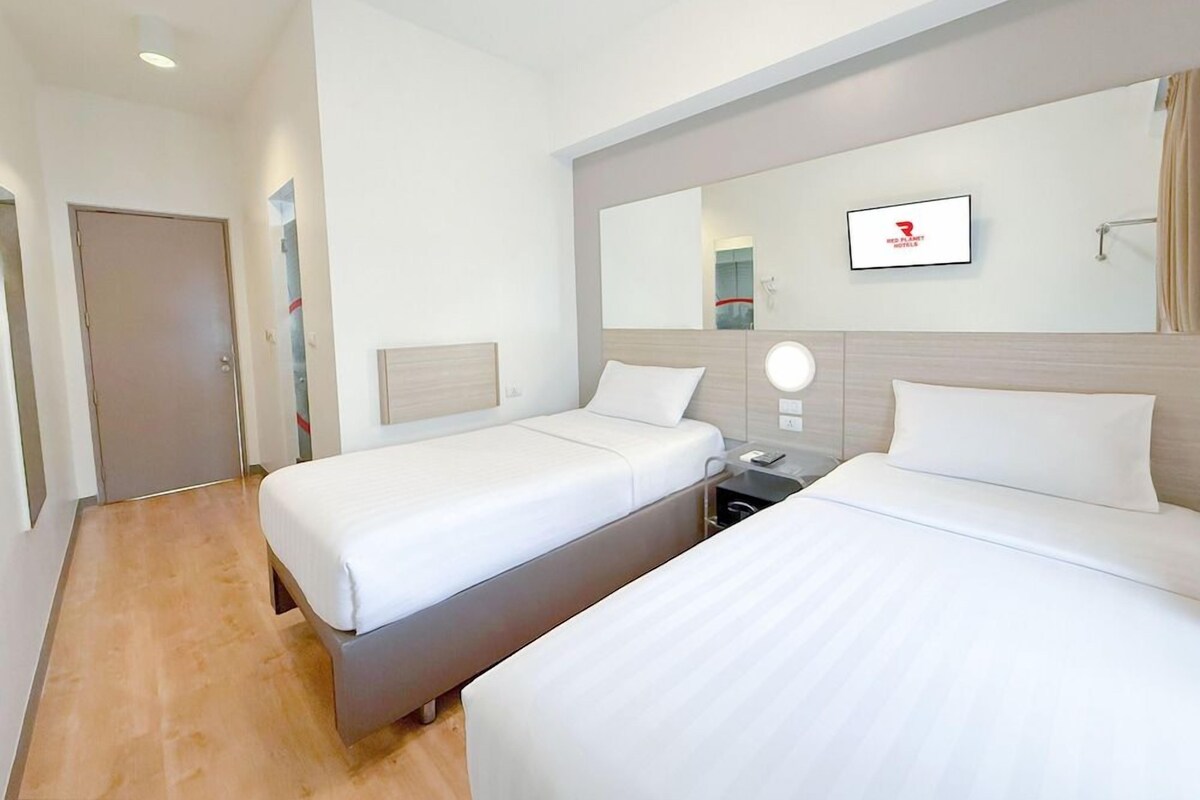 Une chambre d’hôtel avec deux lits, une table de chevet avec une lampe, un miroir et une porte.