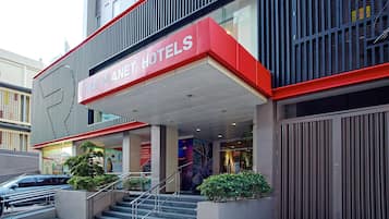 Una entrada de hotel moderna con un letrero llamativo, una escalera y un camino de acceso con portones.