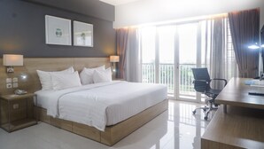 A modern hotel room with a large bed, a desk, and a view of the city through the balcony. - TreePark Karawang (Karawang)