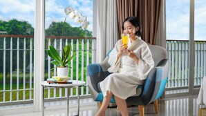A person sitting on a blue and white armchair on a balcony with a potted plant and books on a small table. - TreePark Karawang (Karawang)