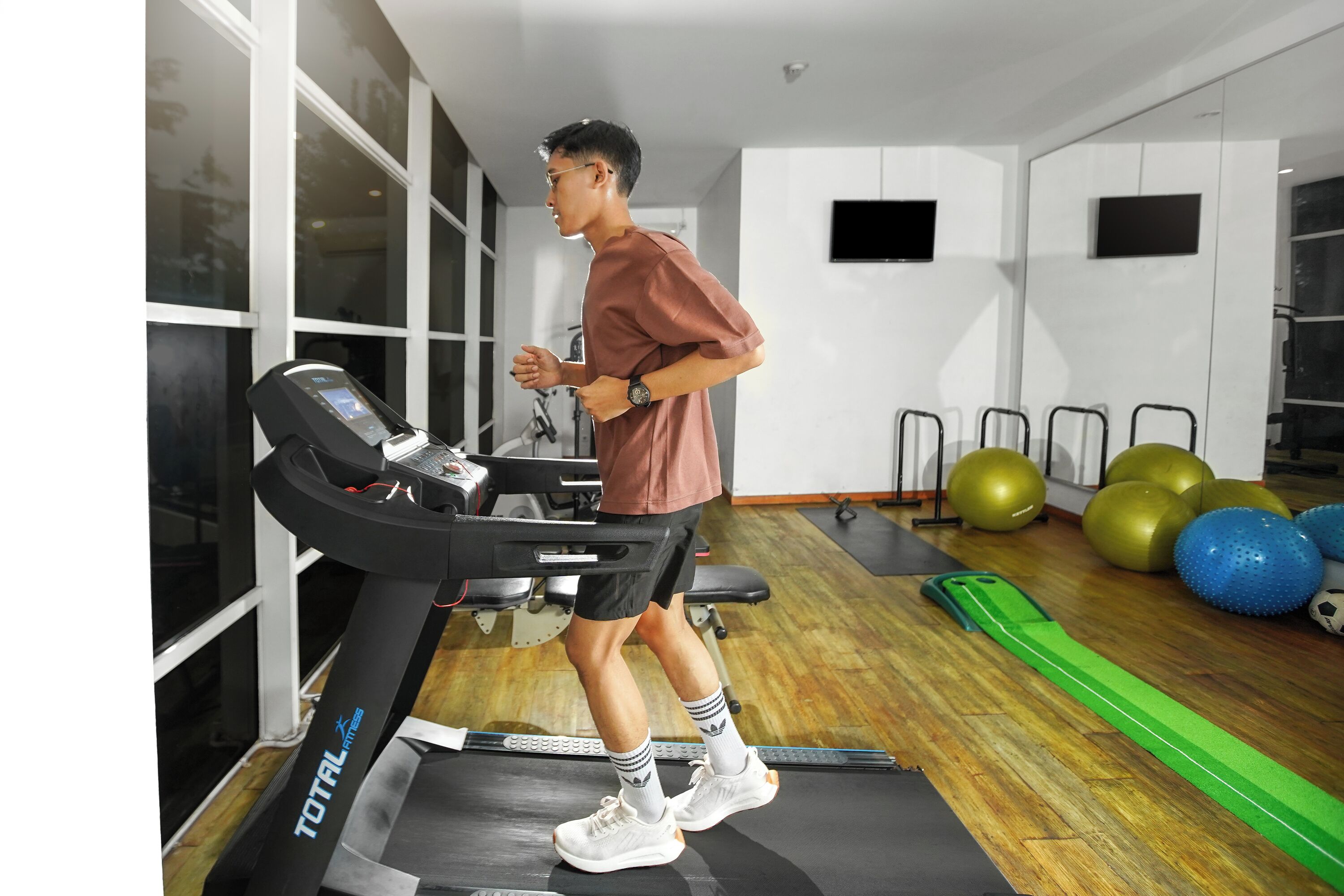 A gym with a treadmill, exercise balls, and a green mat.