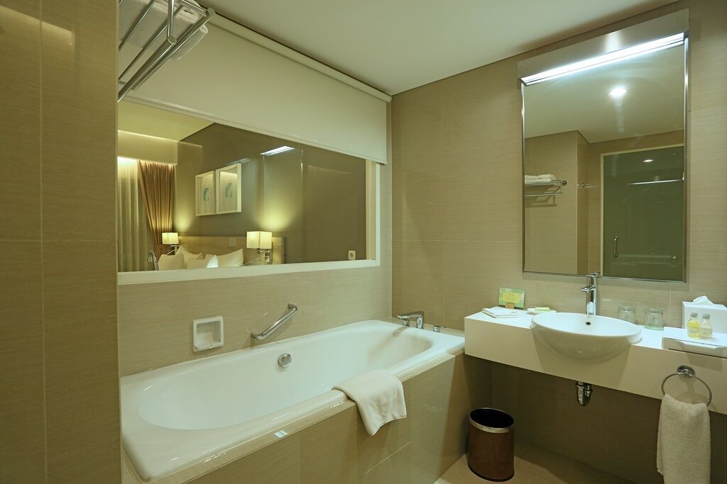A modern bathroom with a bathtub, two sinks, a large mirror, and a trash bin.