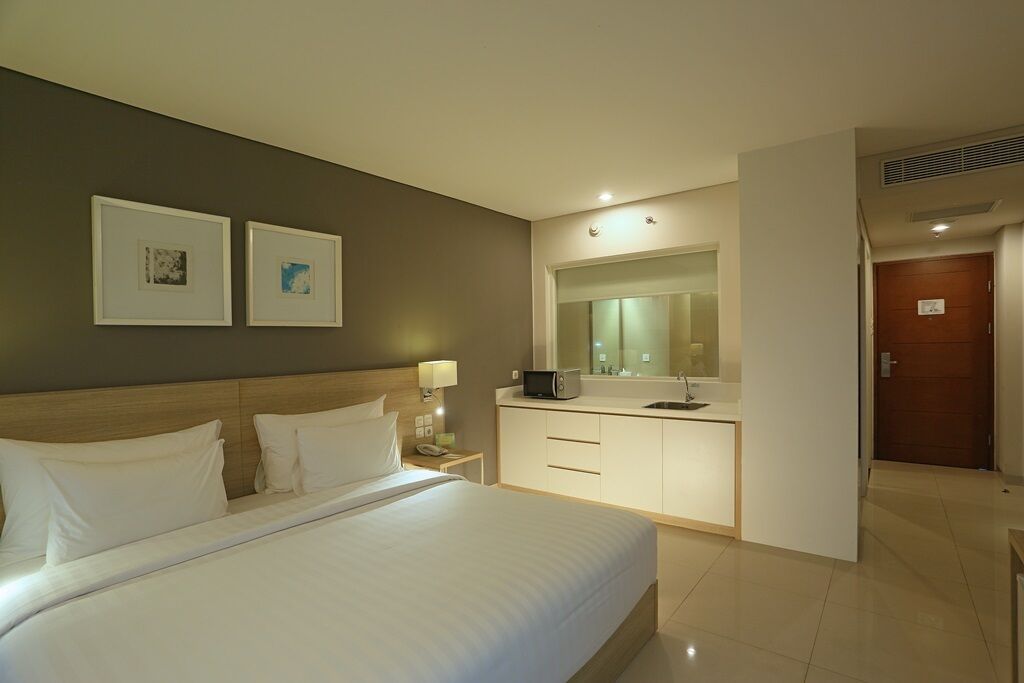 A hotel room with a large bed, a bedside table with a lamp, a small TV, a mirror above the sink, and two framed pictures on the wall.