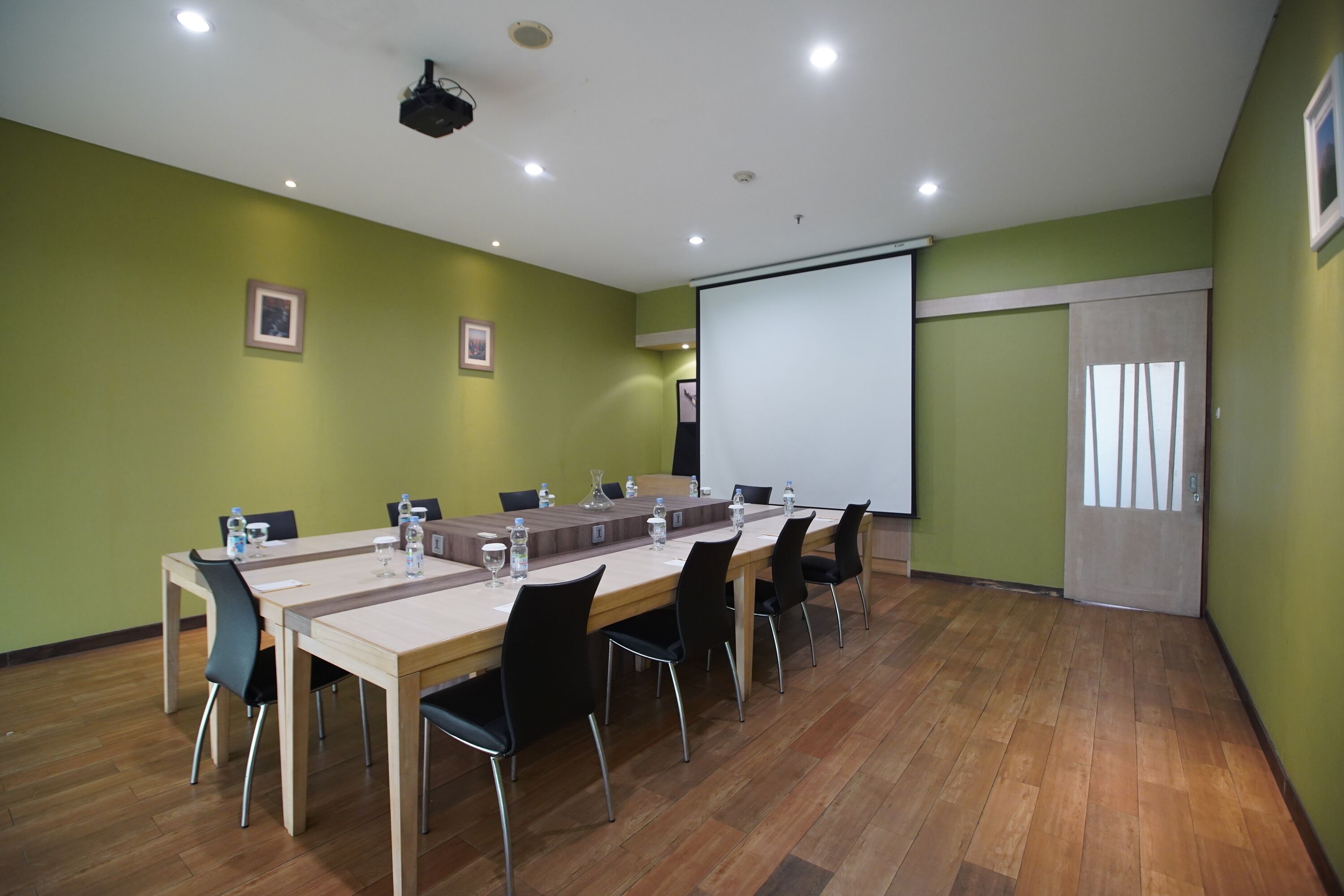 A conference room with a long table, chairs, a projector, and a screen.