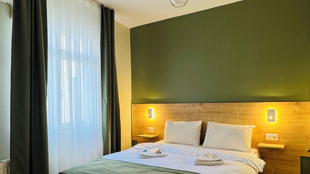 Quarto de hotel com cama de madeira, paredes verdes e duas luminárias de cabeceira.