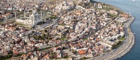An aerial view of a coastal city with a prominent mosque, dense urban area, and a waterfront promenade.