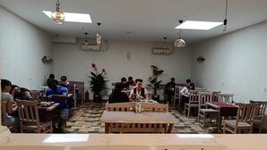 Uma  área de refeições com mesas, cadeiras e um banco central, além de plantas em vasos.