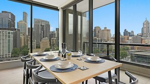 A dining area with a table set for four, large windows offering a city view, and modern chairs. - Corporate Keys - Freshwater Place (Southbank)