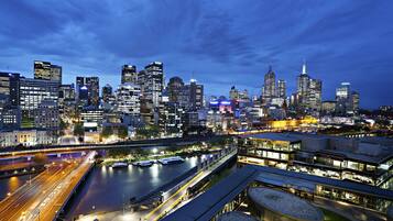 A city skyline at dusk with illuminated buildings and a river with boats.