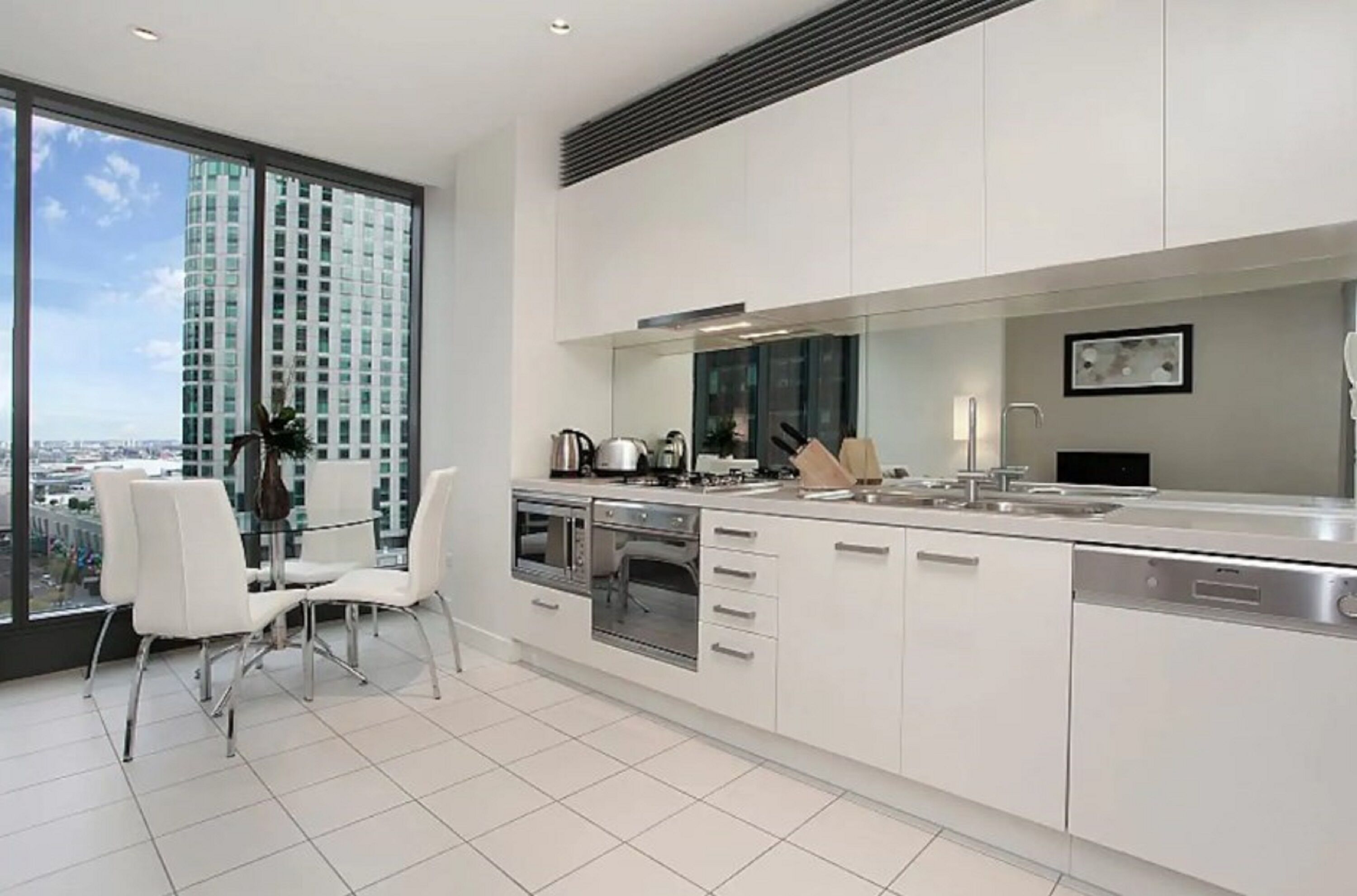 A modern kitchen with white cabinetry, a built-in oven, and a large window offering a city view.