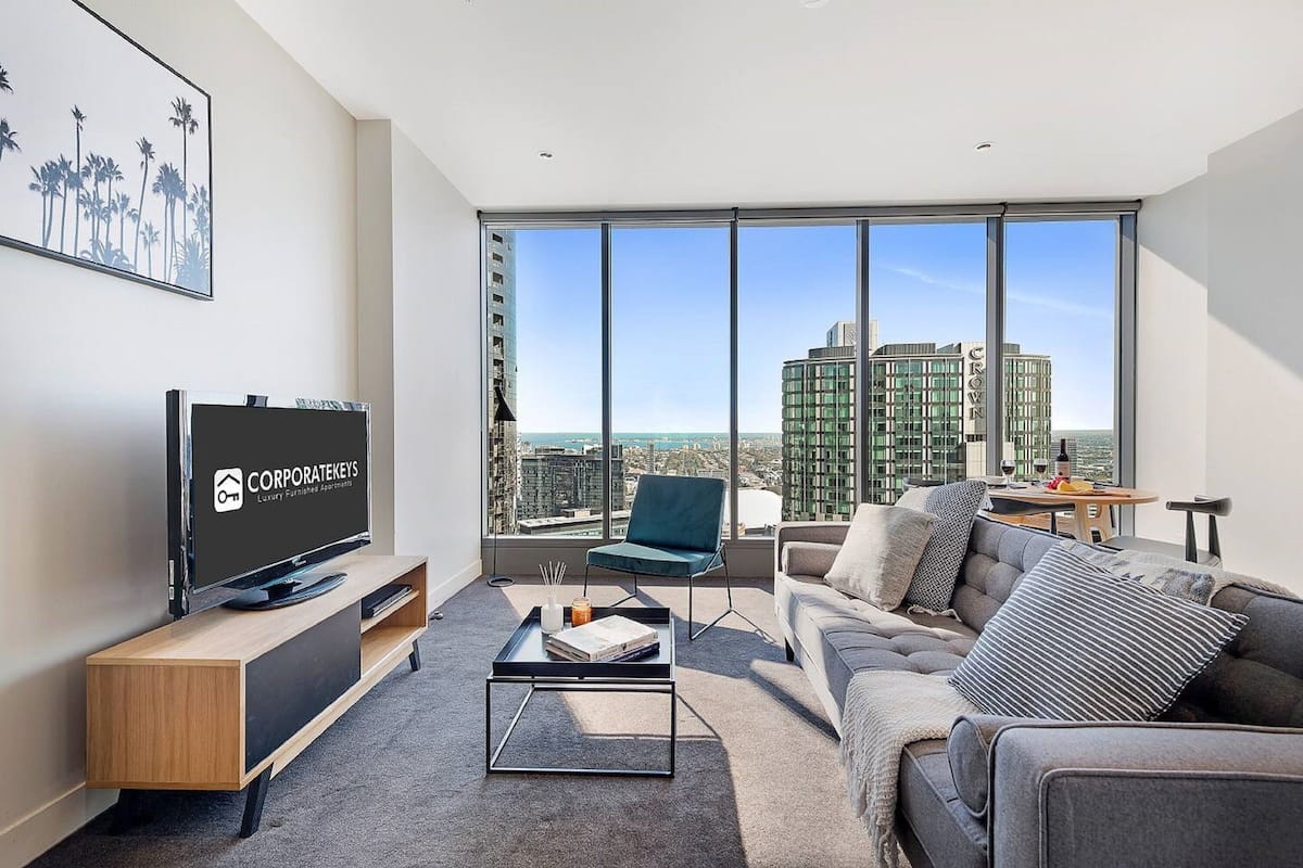 A modern living room with a large window, a flat-screen TV, a sofa, a coffee table, and a chair.