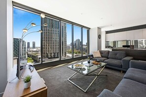 A modern living room with a large window, a sofa, a coffee table, and a desk with a lamp and a plant.