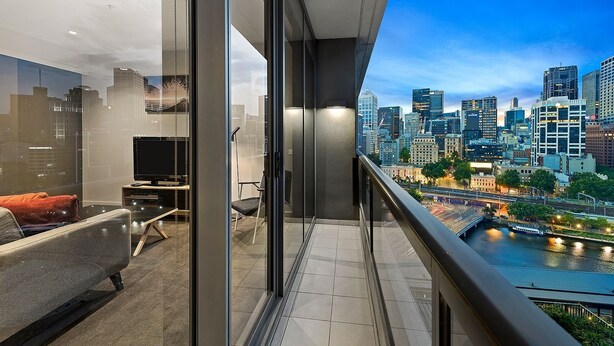 A modern balcony with a city view, a sofa, a TV, and a glass door. - Corporate Keys - Freshwater Place (Southbank)