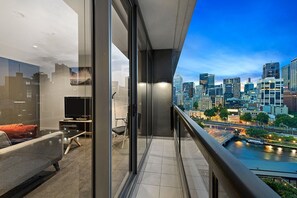 A modern balcony with a city view, a sofa, a TV, and a glass door. - Corporate Keys - Freshwater Place (Southbank)