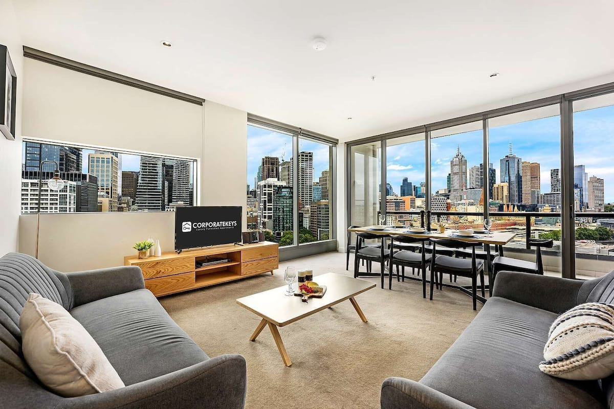 A modern living room with a city view, a flat-screen TV, a dining area, and a sofa.