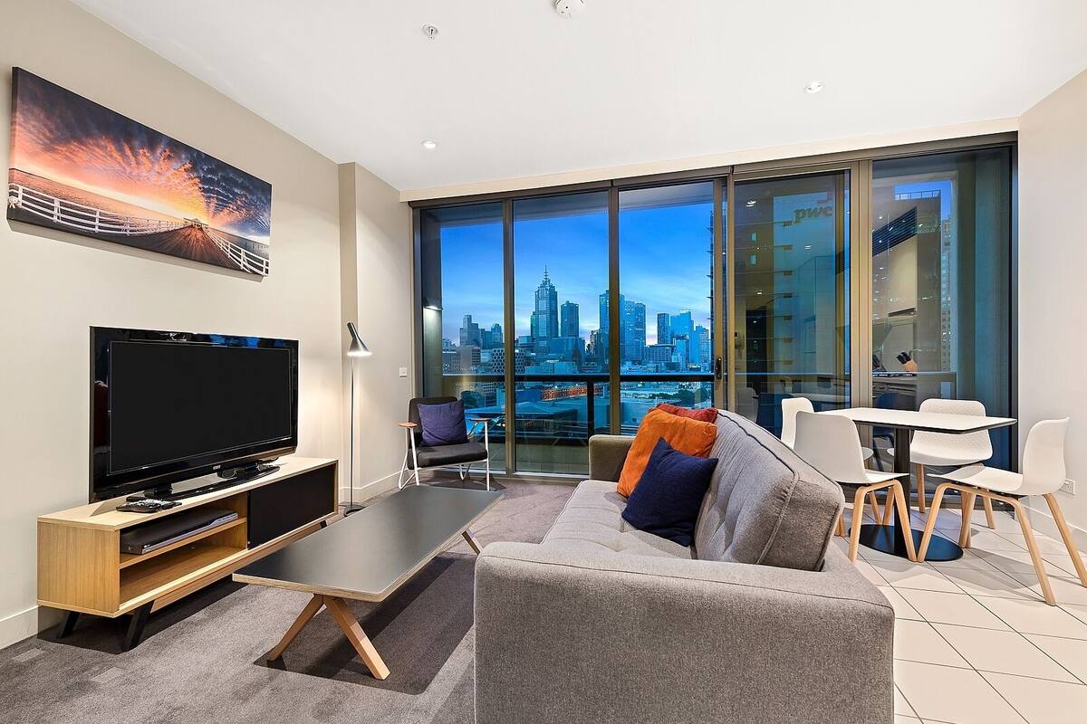 A modern living room with a flat-screen TV, a sofa, a coffee table, and a dining area with chairs.