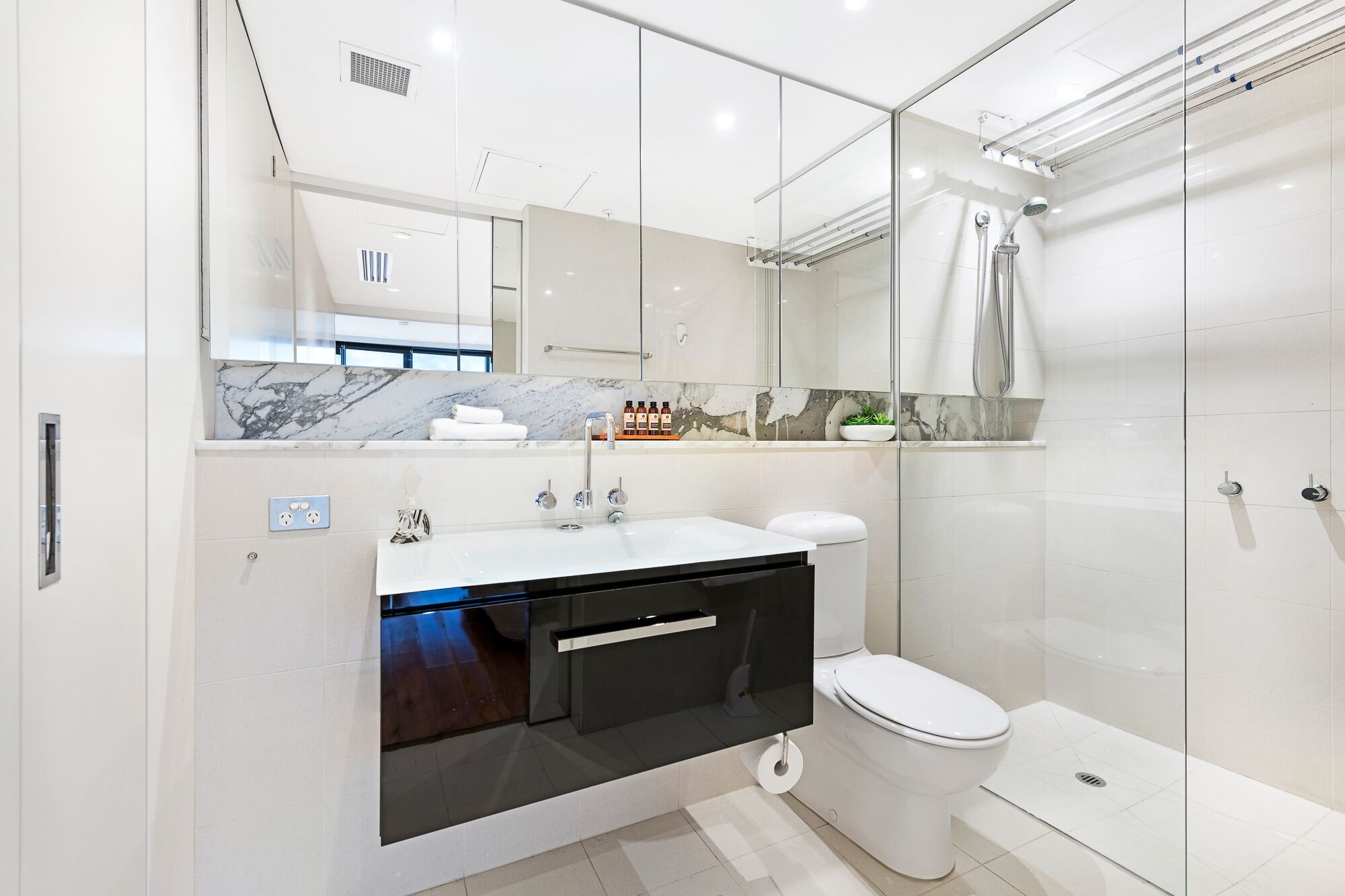 Ein modernes Badezimmer mit Duschkabine aus Glas, einer weißen Toilette und einem Waschtisch mit Marmorplatte.