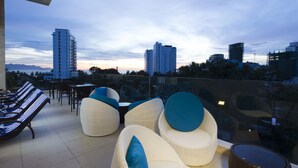 A rooftop terrace with lounge chairs and a glass balustrade overlooking a cityscape. - Dendro Gold Hotel (Nha Trang)