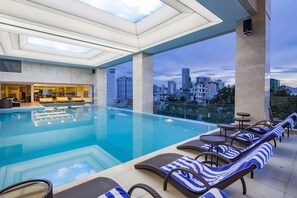 A modern indoor swimming pool with lounge chairs and a city view. - Dendro Gold Hotel (Nha Trang)