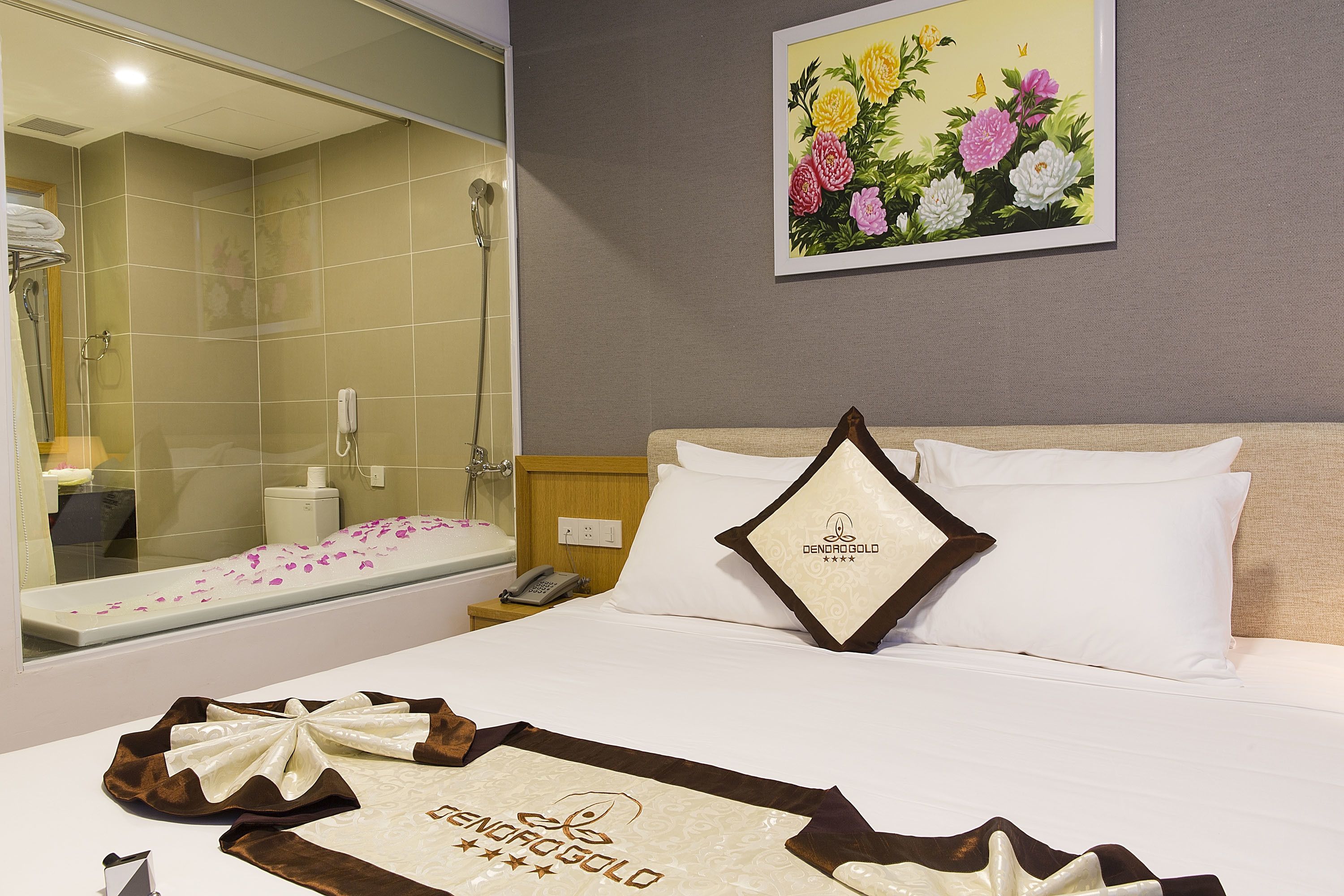 A hotel room with a bed, a nightstand, a mirror, a shower area, and a painting of flowers on the wall.
